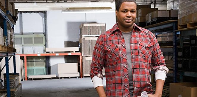 African-American man in a red plaid shirt standing in a warehouse.